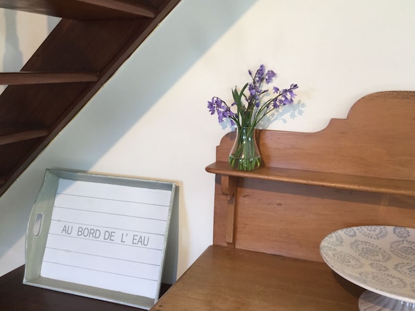 A wooden bench with a vase of purple flowers, a table with a patterned bowl, and a sign with text.