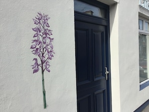 A building with a dark blue door and a purple floral mural on the wall.
