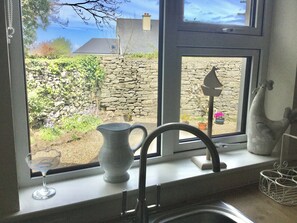 A kitchen window with a stone wall, a potted plant, and a vase.