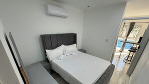 Ein Schlafzimmer mit Bett, Nachttisch und Klimaanlage. Blick auf einen Pool und eine Sitzgelegenheit im Freien.