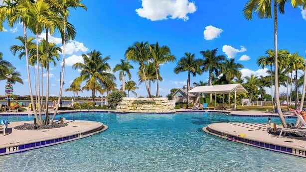 A clear blue pool surrounded by palm trees and a covered pavilion. - Luxurious 2+ BR villa:highly sought after Naples Reserve for annual & seasonal (Naples)