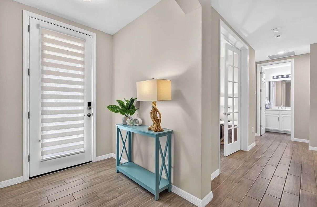 A hallway with a white door, a blue console table with a lamp, a plant, and a decorative piece.