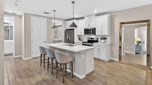 A modern kitchen with white cabinetry, a central island with bar stools, stainless steel appliances, and pendant lighting. - Luxurious 2+ BR villa:highly sought after Naples Reserve for annual & seasonal (Naples)