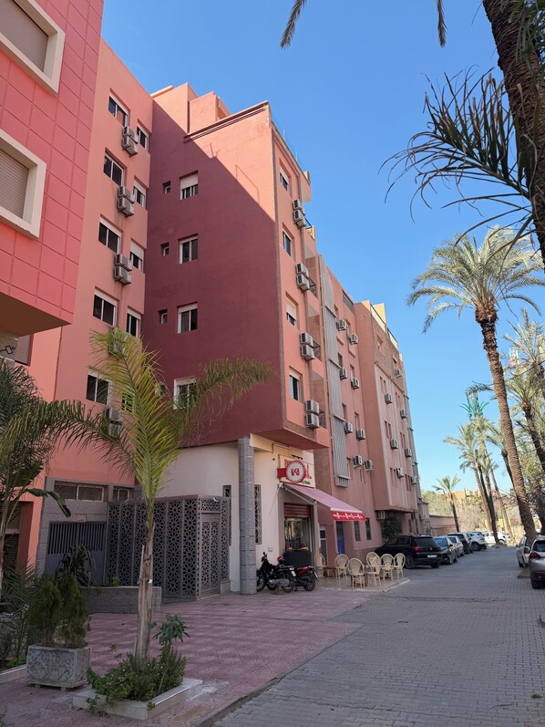 Un edificio de varios pisos con balcones, una entrada protegida por una reja y un pequeño espacio al aire libre con sillas.
