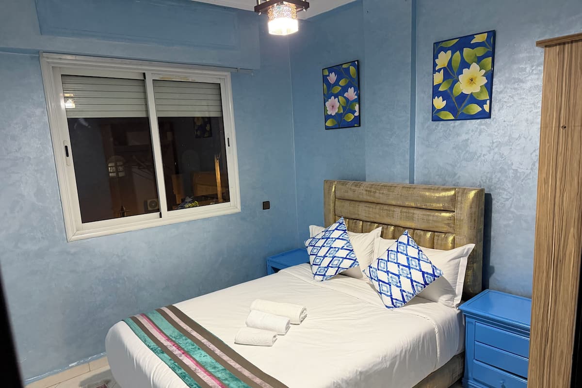 A bedroom with a bed, a window, and two wall paintings.