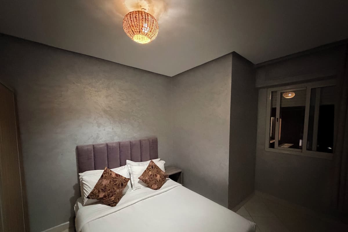 A bedroom with a bed, two pillows, a headboard, a nightstand, and a hanging light fixture.