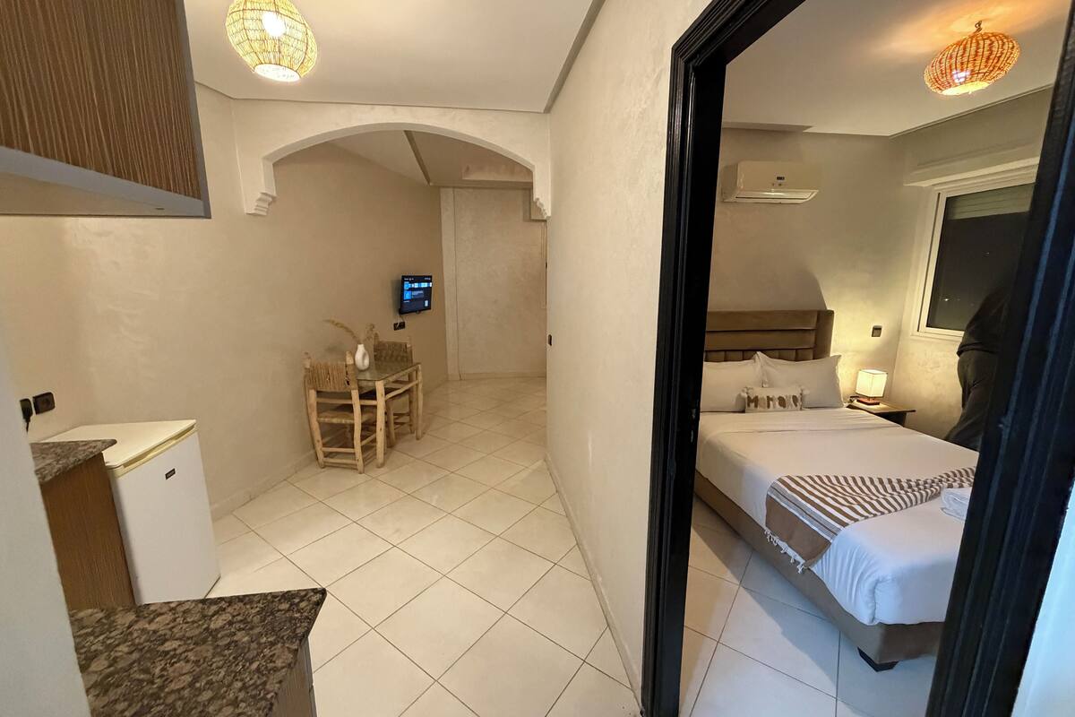 A hotel room with a bed, bedside table, lamp, and a TV mounted on the wall.