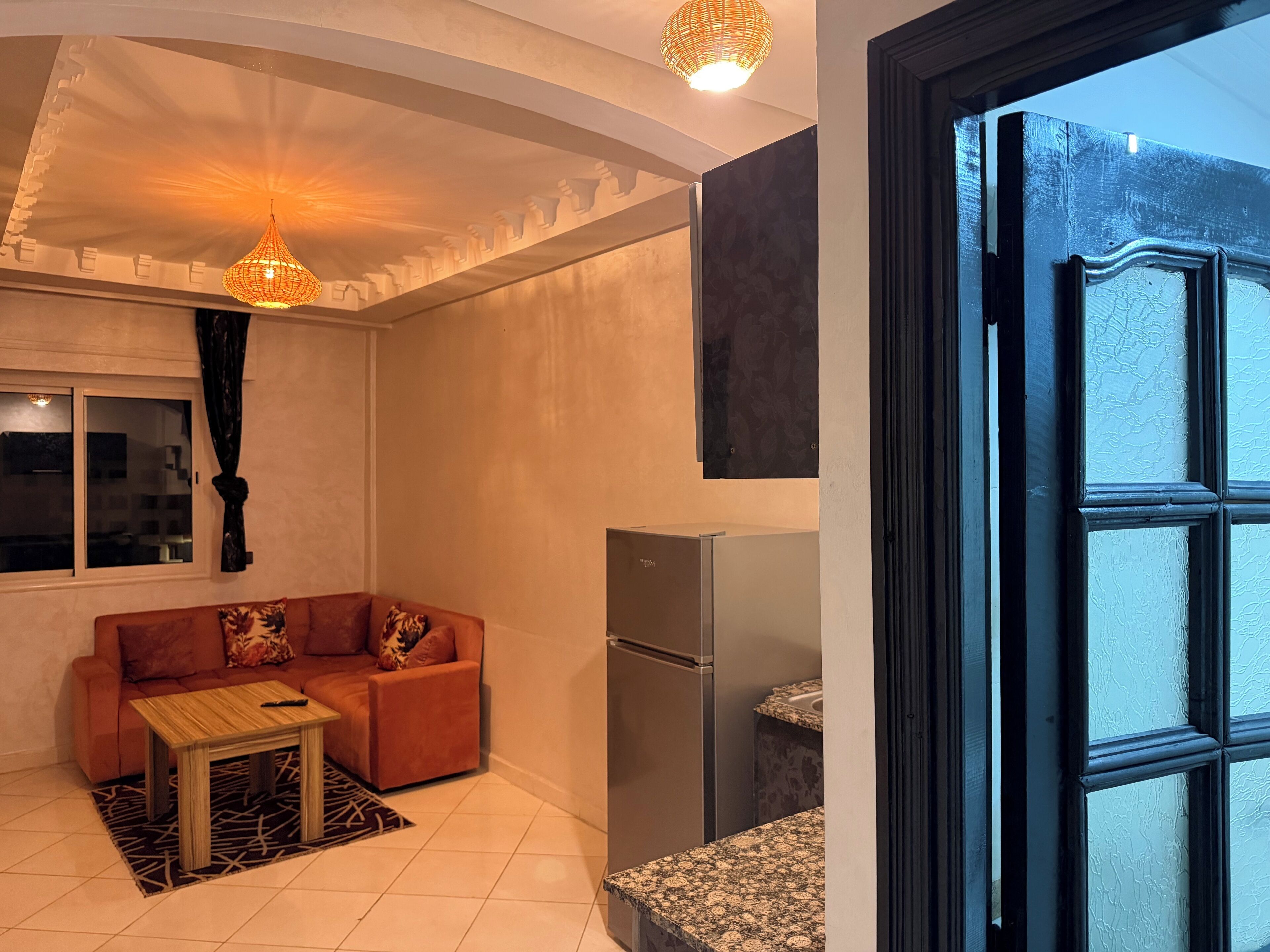 Ein kompakter Wohnbereich mit einer Couch, einem kleinen Tisch, einem Kühlschrank und einem Fenster mit Blick.