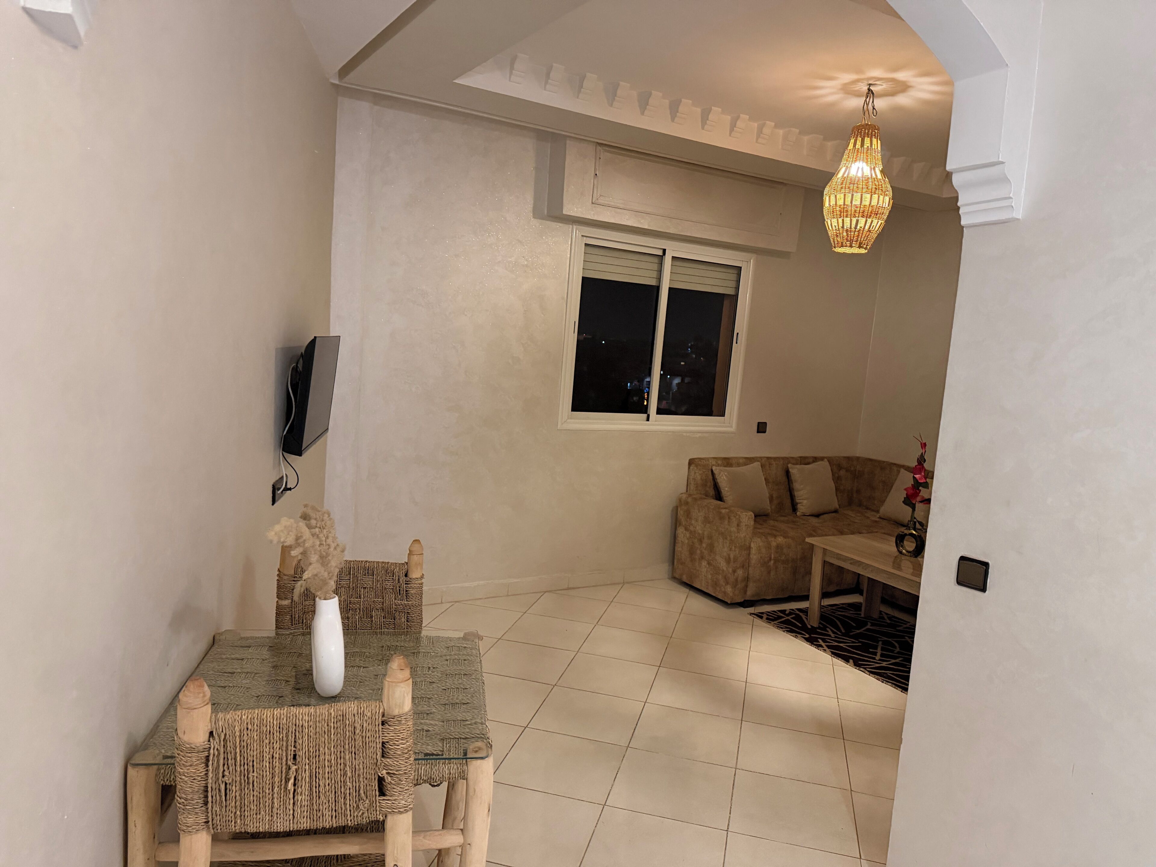 Una sala acogedora con un sofá, una mesa de comedor con sillas, un florero y una lámpara colgante.