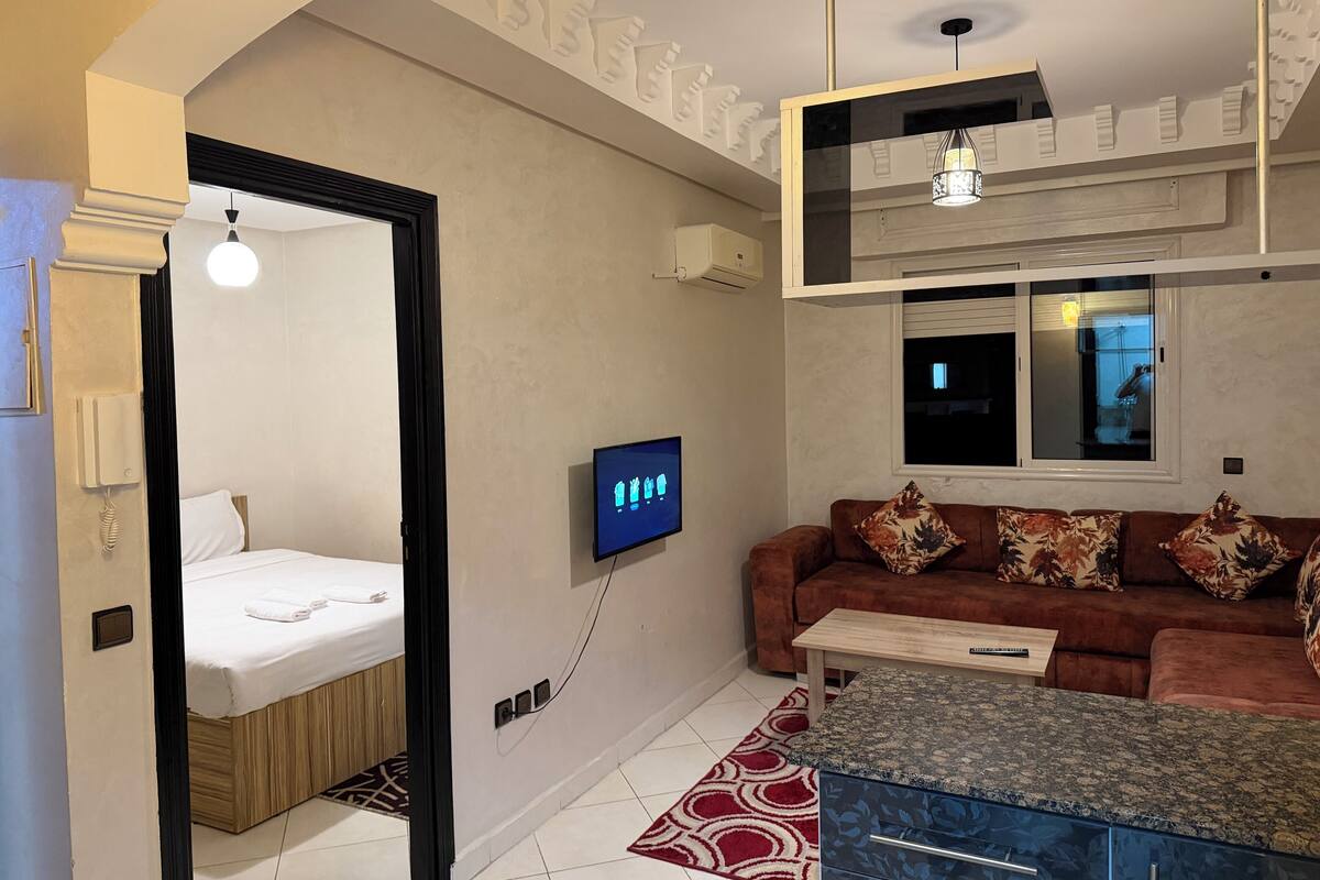 A modern hotel room with a bed, a sofa, a TV, and a small table.