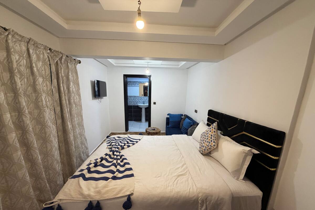 A bedroom with a bed, a TV, a window, and a door leading to a bathroom.