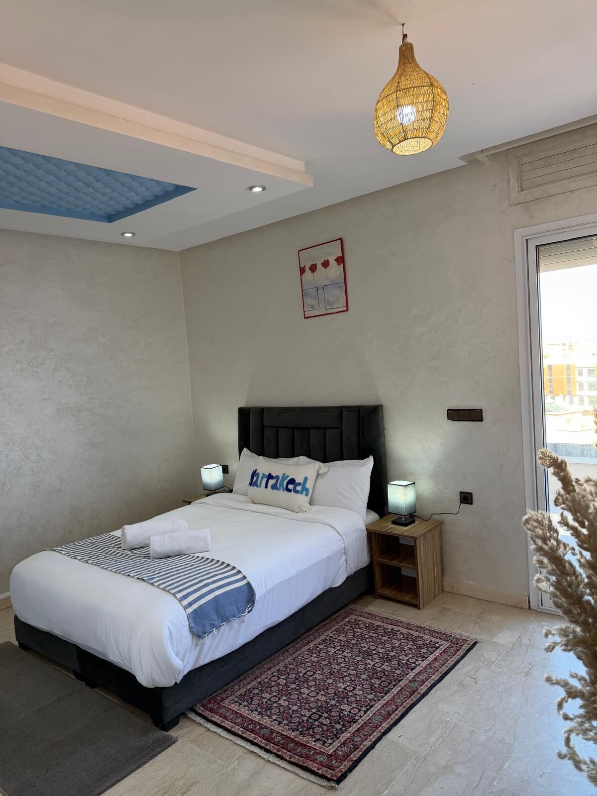 A bedroom with a bed, bedside lamps, a decorative wall piece, and a hanging light fixture.