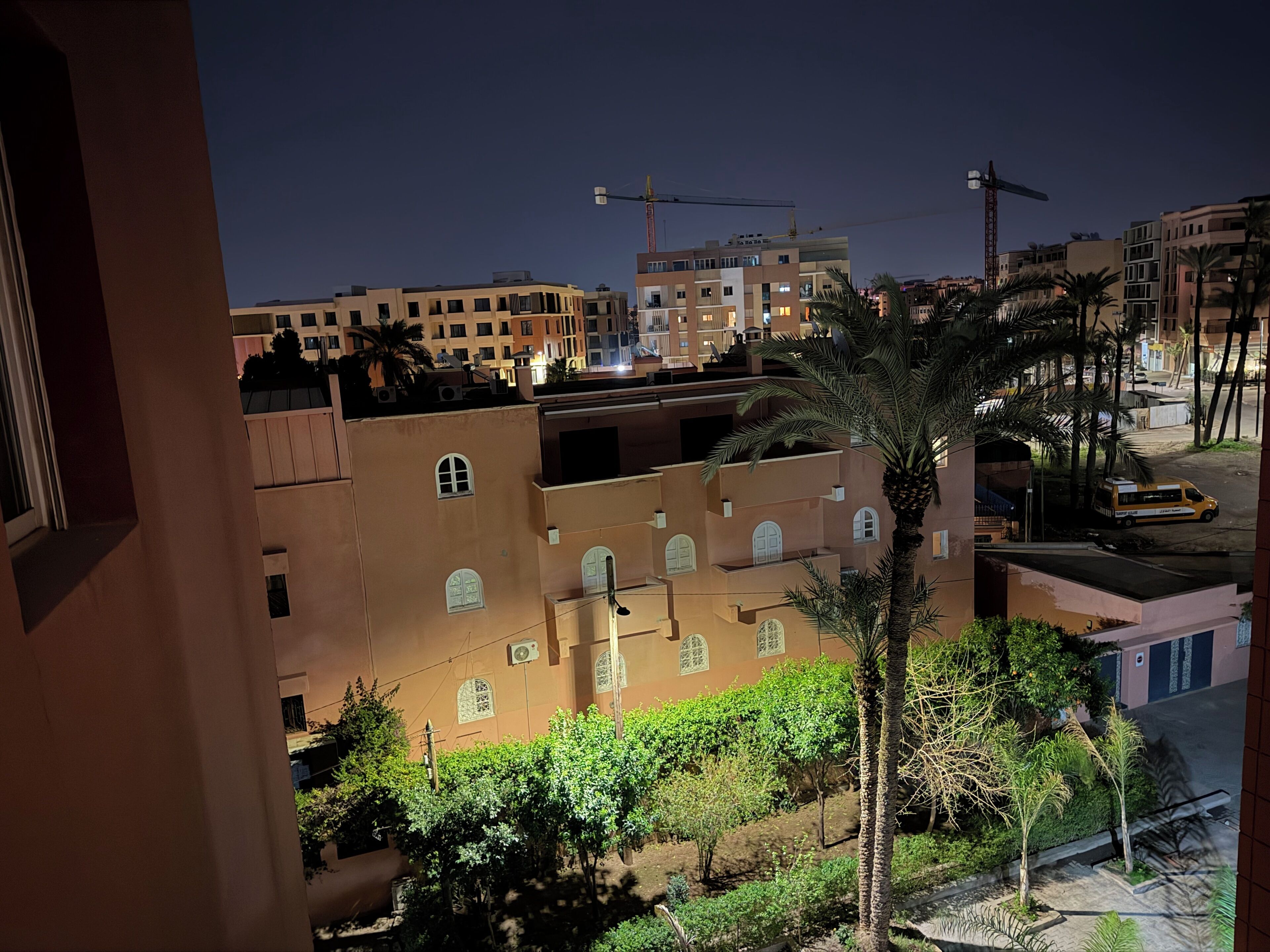 A view of a residential area with multi-story buildings, palm trees, and a construction crane in the background.