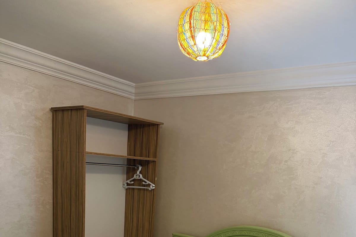 A neatly made bed with white linens and two rolled towels, a green headboard, and a wooden wardrobe with a mirror and a hanger.