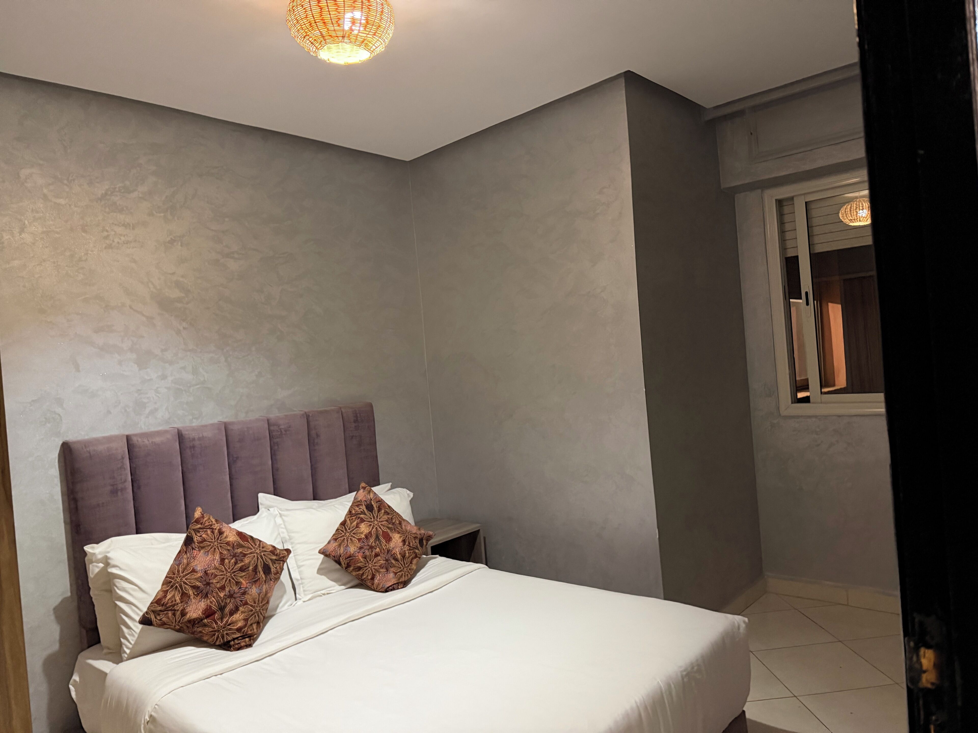 A bedroom with a large bed, a headboard, and a window with a view.
