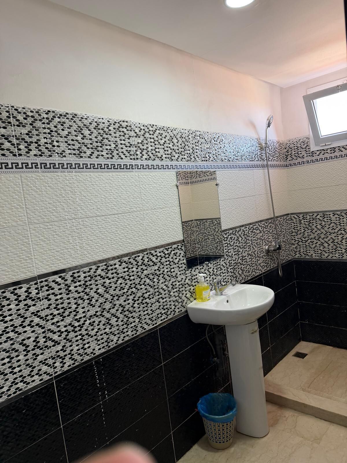 A bathroom with black and white patterned tiles, a white sink, and a blue trash bin.