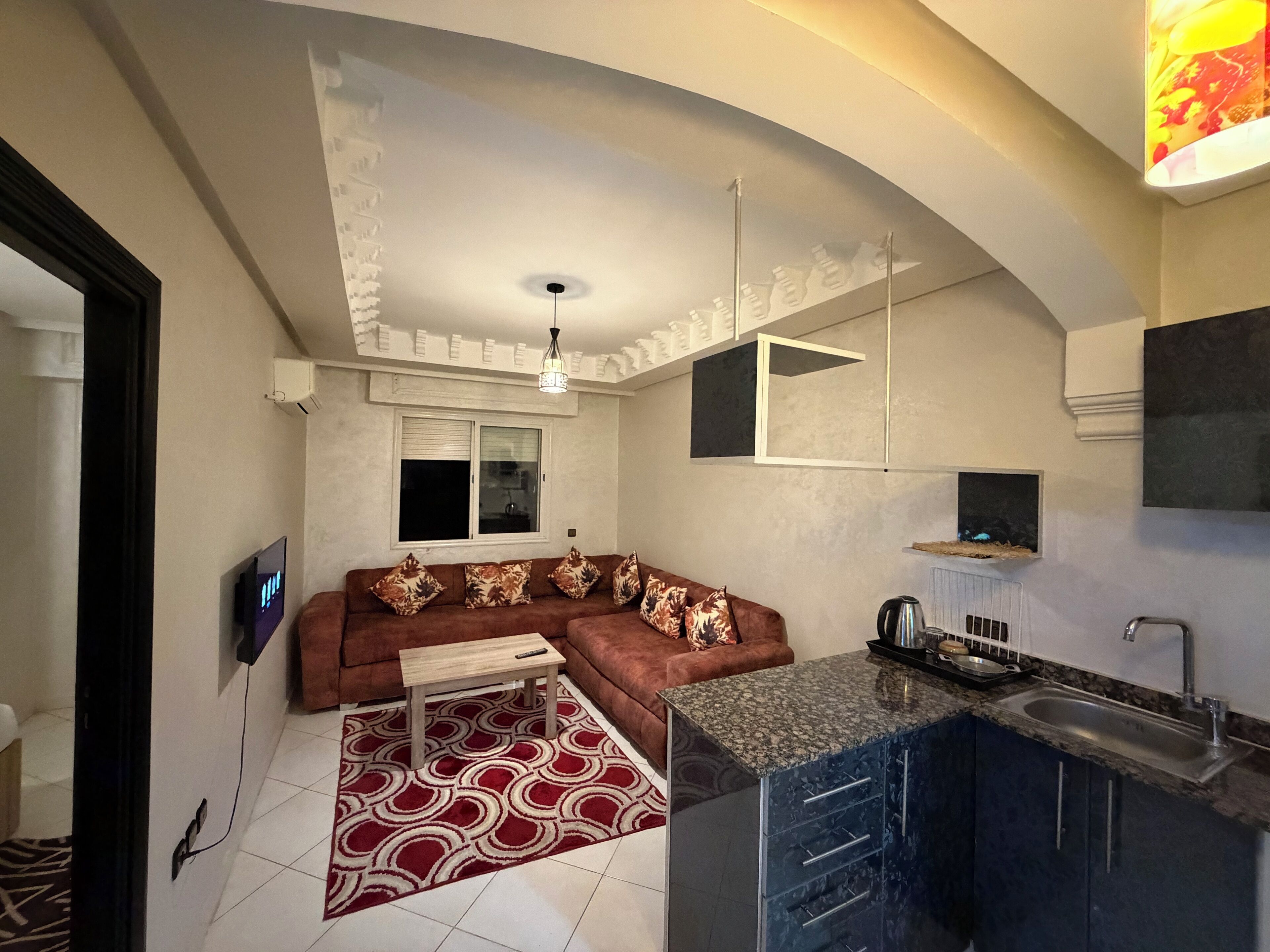 Un espacio habitable compacto con sofá, una mesita, una zona de cocina con fregadero y una lámpara en el techo.