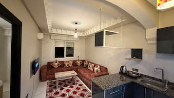 Un espacio habitable compacto con sofá, una mesita, una zona de cocina con fregadero y una lámpara en el techo.