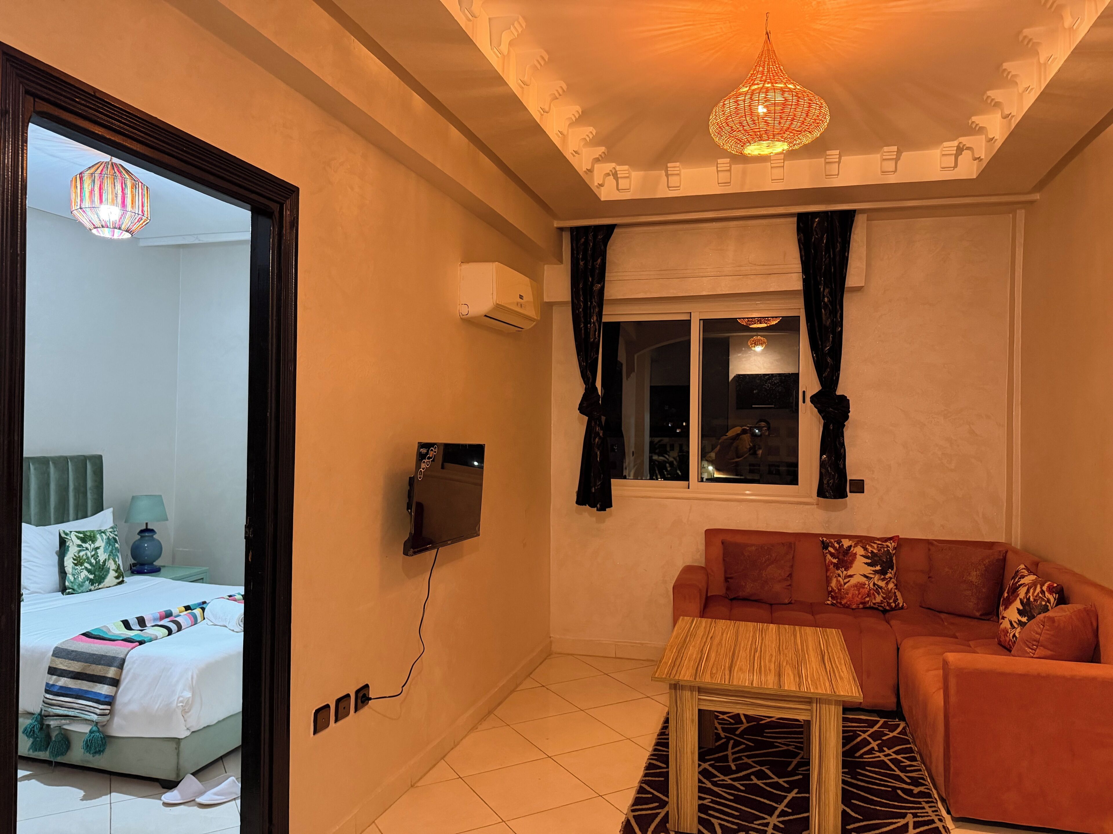Una habitación con una cama, un sofá, una mesita, un televisor y un ventanal con cortinas.