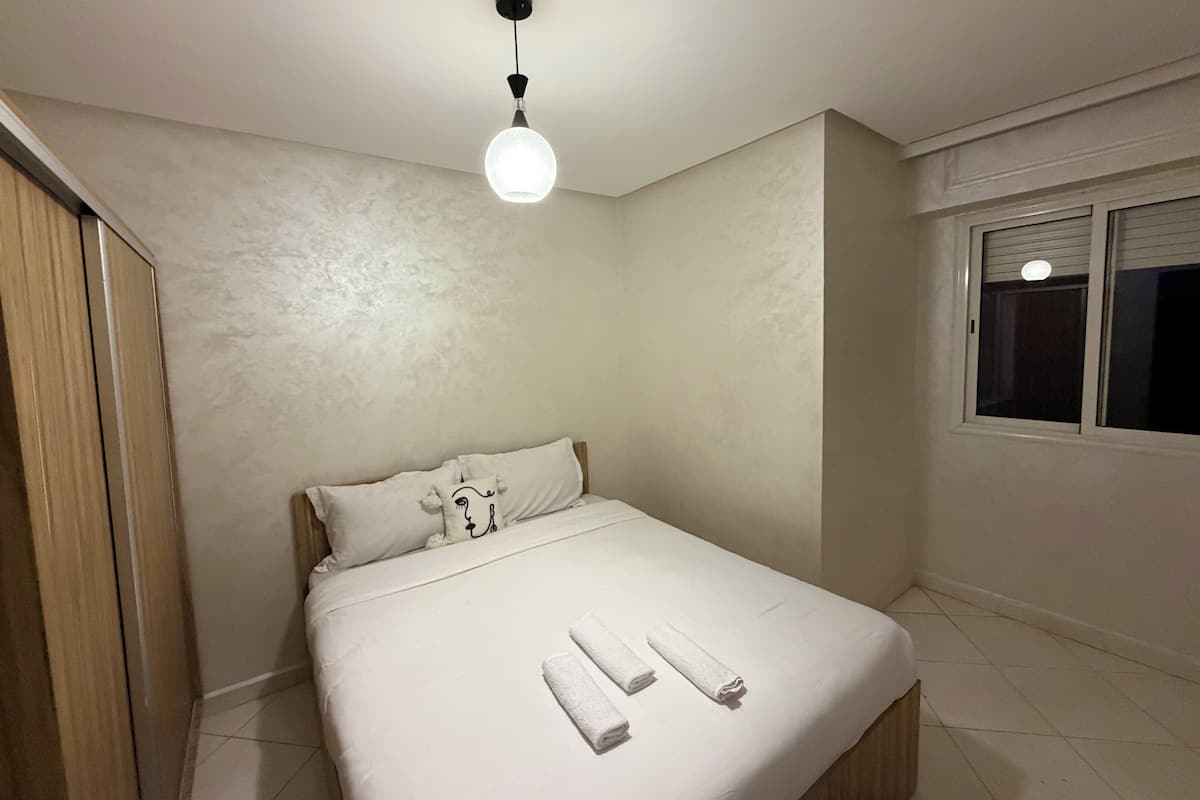 A neatly made bed with white linens and towels, a single pillow, and a hanging light fixture.