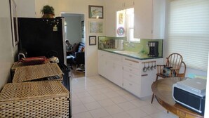 A compact kitchen with white cabinets, a black refrigerator, wicker baskets, a wooden table, and a window with blinds. - Cozy 1-bedroom sunset beach apartment in San Diego (San Diego)