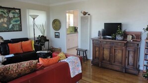 A living room with a red sofa, a black armchair, a floor lamp, a television, and a cabinet with decorative items. - Cozy 1-bedroom sunset beach apartment in San Diego (San Diego)