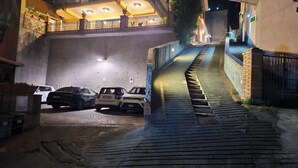 A narrow alleyway with a staircase leading up to a building. There are parked cars on the left side and a gated entrance on the right. - Taormina Home La Terrazza di Fede. 5 minutes walk from downtown. Private car park (Taormina)
