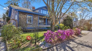 Ein zweistöckiges Haus mit blauer Fassade und einem Garten mit lila Blumen.