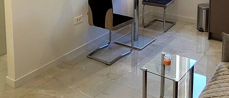 Una sala de estar moderna con una televisión de pantalla plana montada en la pared, una mesa de comedor con dos sillas, una mesa de centro de vidrio y un sofá.