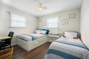 A bedroom with two beds, a desk, a chair, a ceiling fan, and wall-mounted artwork.