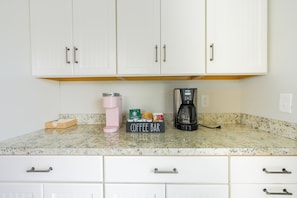 A kitchen with white cabinets, a coffee maker, a pink water bottle, and a sign that reads 'Coffee Bar.'