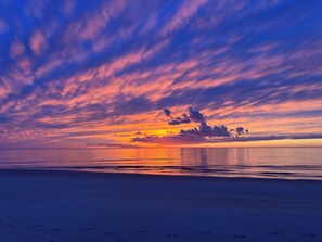 Una playa con huellas que conducen al agua, un atardecer y un cielo despejado.