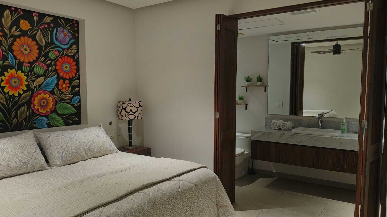 Una camera da letto con un letto, un comodino, una lampada e un quadro floreale dai colori vivaci appeso al muro.