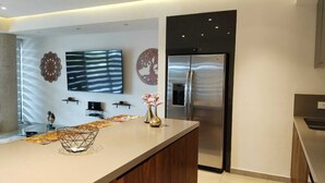 Eine moderne Küche mit einer großen Kochinsel, Edelstahlgeräten, einem flachbildfernseher an der Wand und dekorativer Wandkunst.