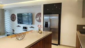 A modern kitchen with a large island, stainless steel appliances, a flat-screen TV mounted on the wall, and decorative wall art. - Romantic Zone, Large 3 Bedroom 3 Bathroom Apartment (Puerto Vallarta)