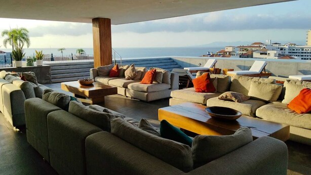 Eine Dachterrasse mit Sofas und Tischen mit Blick auf eine Stadt und das Meer.