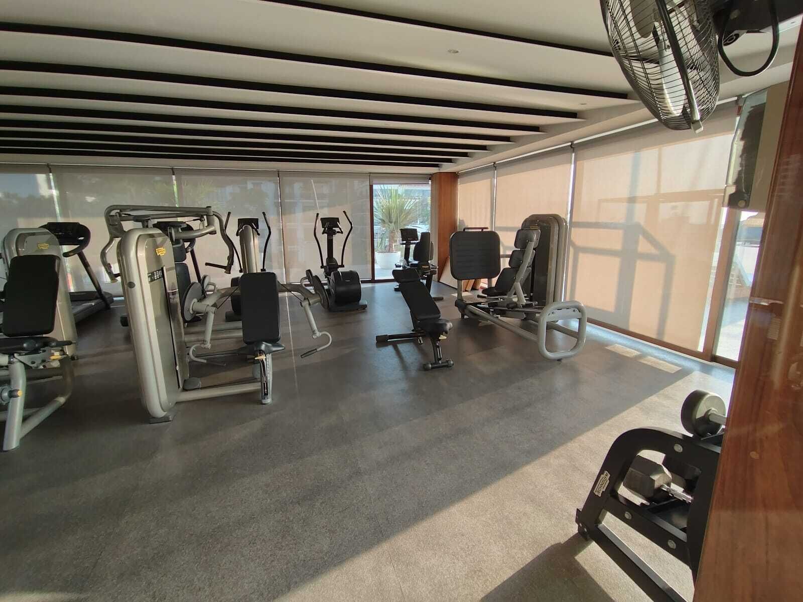 A gym with various exercise equipment, large windows, and a ceiling fan.