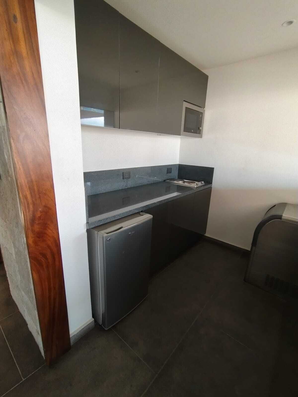 A compact kitchen with dark countertops, a built-in microwave, and a small refrigerator.