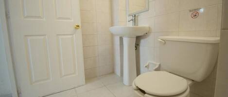 Un baño con inodoro blanco, lavabo y espejo.