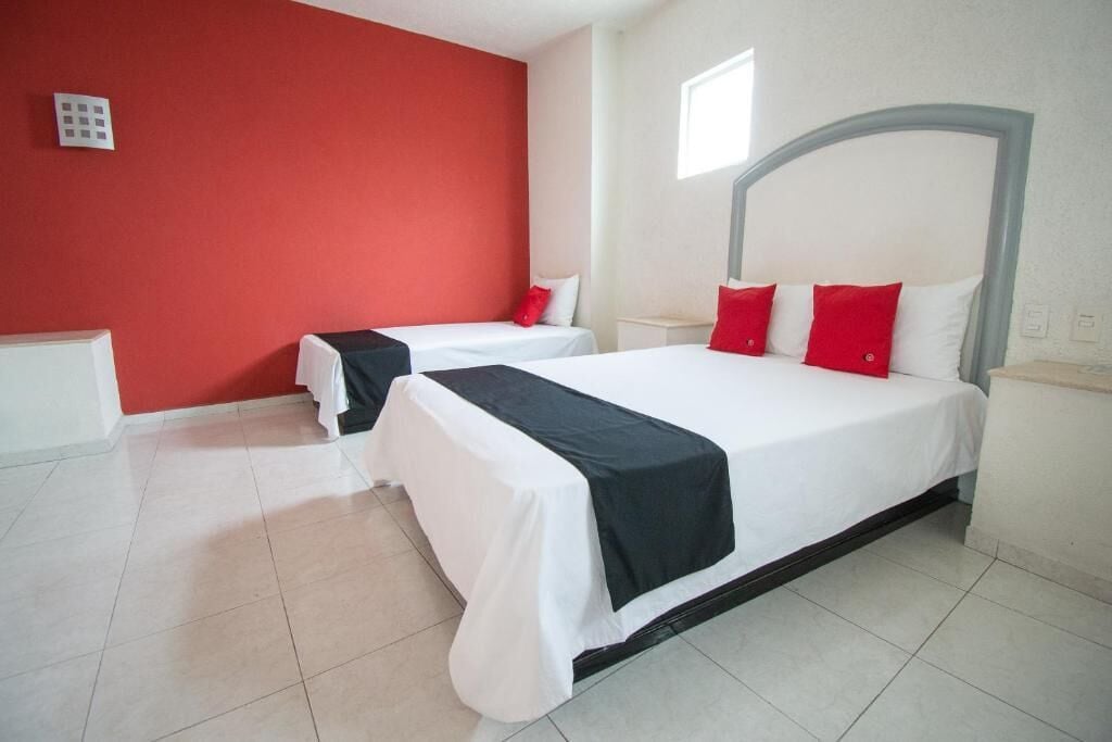 Una habitación de hotel con dos camas, cada una con ropa blanca y almohadas rojas.