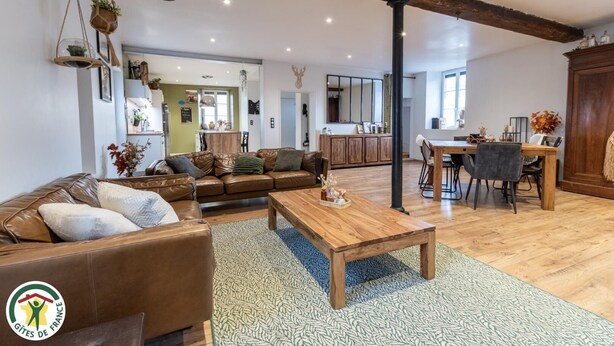 A spacious living room with a leather sofa, wooden coffee table, and a dining area with a wooden table and chairs. - La Forge - BISSEUIL - Gîte (BISSEUIL)