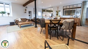 A spacious living area with a wooden dining table, leather sofas, and a kitchen in the background. - La Forge - BISSEUIL - Gîte (BISSEUIL)