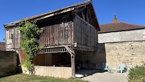 A rustic two-story building with a wooden balcony, a stone wall, and a gravel driveway. - La Forge - BISSEUIL - Gîte (BISSEUIL)