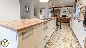 A modern kitchen with a wooden countertop, white cabinets, and patterned floor tiles. - La Forge - BISSEUIL - Gîte (BISSEUIL)