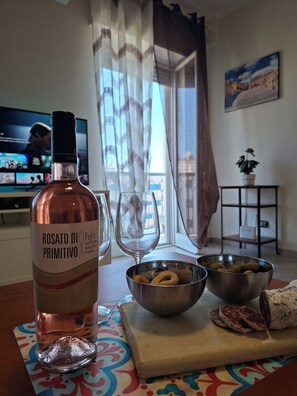 A bottle of Rosato Di Primitivo wine, two bowls of snacks, and a glass of water on a table in a room with a TV and a window with curtains. - La Casa Del Sole, Brindisi. (Brindisi)