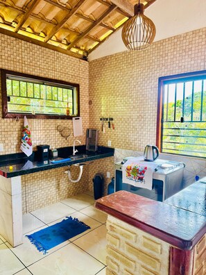 Une cuisine avec un mur recouvert de carreaux, une fenêtre donnant sur un beau paysage, un évier, une cuisinière et un tapis bleu sur le sol.