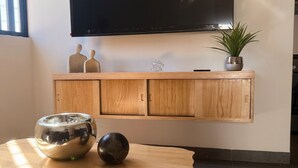 Ein modernes Wohnzimmer mit einem Holzschrank, einem flachbildfernseher an der Wand, einer kleinen Topfpflanze und zwei dekorativen Schalen auf einem Holztisch.