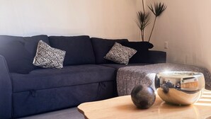 Ein modernes Wohnzimmer mit einem dunkelblauen Sofa, gemusterten Zierkissen, einem Holztisch und einer Zimmerpflanze.