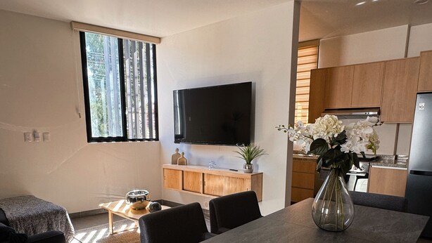 Ein modernes Wohnzimmer mit Essbereich, einem flachbildfernseher an der Wand und einer Küche mit Holzschränken und einem Edelstahlkühlschrank.