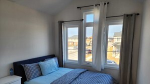 Un dormitorio con cama, mesita de noche y ventana con cortinas.